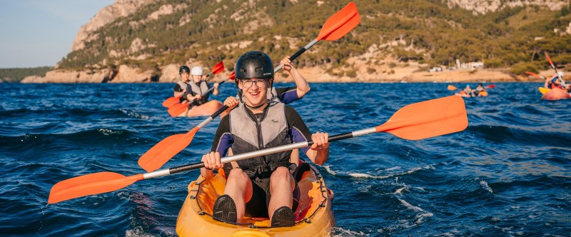 People kayaking in blue water with mountains and trees in the background.