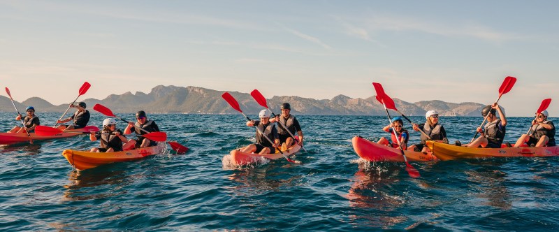 Group of people kayaking in ocean with distant mountains under clear blue sky.