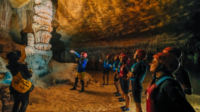 Group of people with helmets and vests exploring a cave with stalactites.