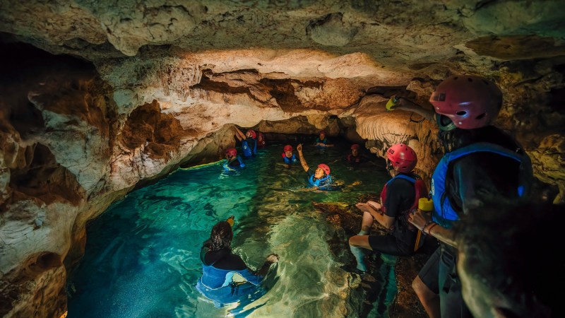 People with helmets and life vests explore a water-filled cave.