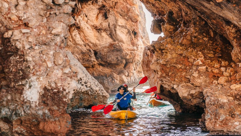 People kayaking through narrow rocky cave with bright colors.